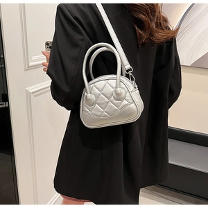 Detail view of a silver quilted shell bag worn crossbody over a classic black blazer