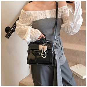 Detail of black glossy square handbag featuring a bow and pearl charm on a model
