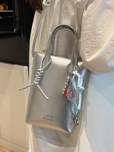 Minimalist metallic silver mini tote bag with tennis racket charm shown in a lifestyle scene