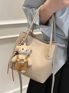 Minimalist beige bucket bag with lychee texture and cute plush bear charm for daily use