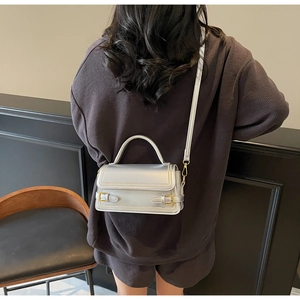 Silver metallic crossbody bag with dual buckles shown worn by a model in detail view