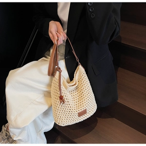 Détail du sac seau en tricot avec bandoulière en cuir marron et écusson logo en été
