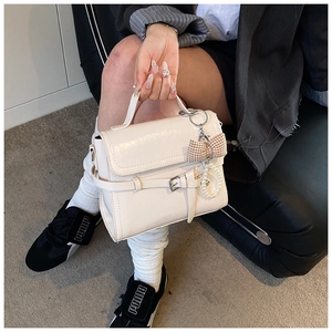 Detail of cream leather handbag featuring buckle strap and pearl bow charm accessory