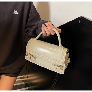 Detailed view of beige rectangular handbag with scalloped edges and gold buckle straps