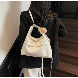 Detail of white leather tote bag featuring a pink pompom, silk scarf, and chain strap accent