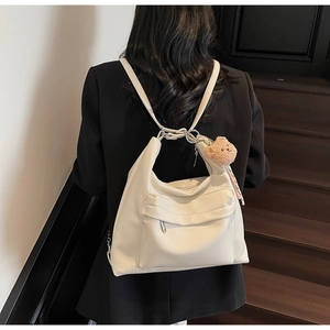 Close-up of cream soft leather tote bag featuring a plush bear charm and zipper pocket