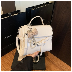Detail of white glossy leather handbag with bow, pearl charms and metal heart pendant