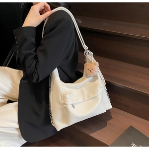 White faux leather crescent tote bag detail with plush bear charm and chain strap