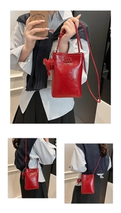 Detail of red patent leather phone bag with embossed m logo and matching accessory charm