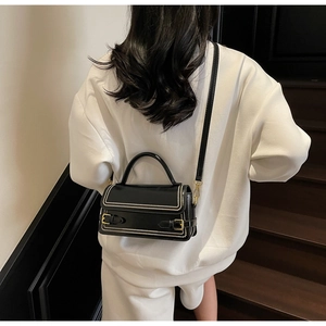 Detail view of black patent leather crossbody bag with pearl trim and gold hardware accents
