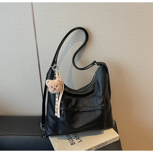 Detail shot of black litchi pattern leather tote bag with front pocket and plush bear charm