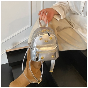Detail of silver mini backpack with gold paw and bone metal studs being held by model