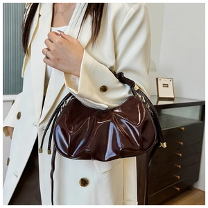 Detail of a dark brown pleated cloud bag with shiny oil-wax finish and gold buckle