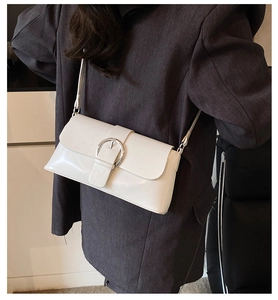 Close-up of white rectangular shoulder bag with large silver metal buckle on grey coat