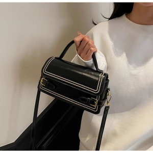 Detail view of black glossy leather crossbody bag featuring gold studs and buckle straps