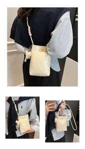 Close-up of beige rectangular phone bag with metal M logo and cute elephant charm accessory