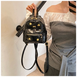 Close-up of mini black patent leather backpack with gold rivets and bone charm detail