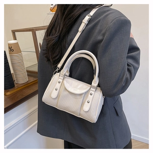 Detail der weißen gesteppten Zylindertasche mit Nieten, getragen über grauem Blazer