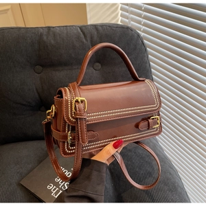 Detail of brown faux leather handbag featuring gold studs and decorative buckle strap