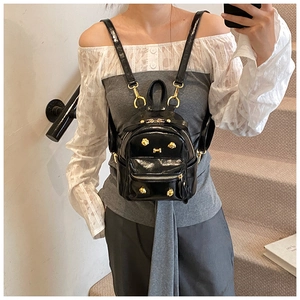 Detail of a black mini backpack with gold bear-shaped rivets on glossy patent leather