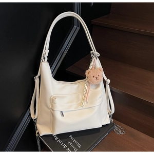 Detail view of cream hobo tote bag featuring a plush bear charm and leather tassels