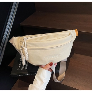Detail view of cream canvas waist bag with embroidered logo and orange side label on wood steps