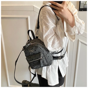Detail of grey polka dot mini backpack featuring a decorative metal bow and front pocket