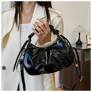 Detail of black glossy pleated cloud bag featuring gold-tone zippers and adjustable hardware