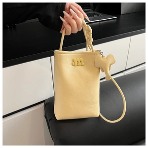 Detail of warm yellow PU leather phone bag with m-logo, elephant charm and woven handle