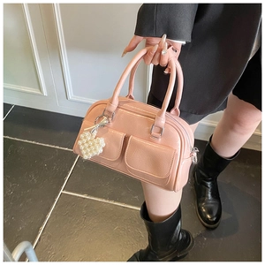 Detail of pink glossy Boston bag featuring front pockets and pearl heart pendant
