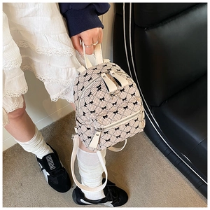 Detail of a beige quilted mini backpack with black bow print and gold zipper finish