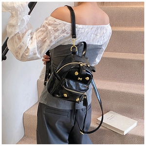 Detail of a mini black glossy backpack with golden bone hardware and stud accents