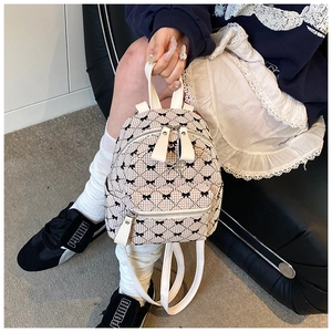 Close-up of beige quilted mini backpack with black bow pattern and silver metallic detail