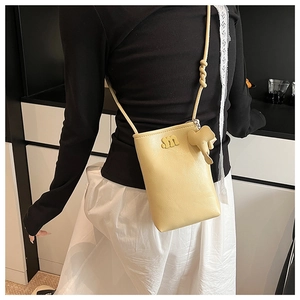 Detail of cream crossbody phone bag with gold 'm' logo, elephant charm and knotted strap