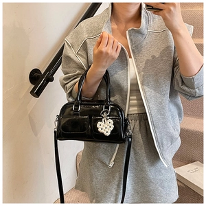 Detail of glossy black Boston bag with a pearl heart charm on a grey knit outfit