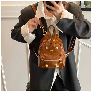 Brown mini puppy backpack with gold studs and bone charms worn as a stylish chest bag