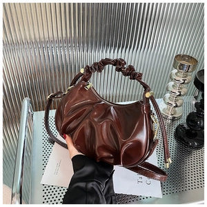 Detail of a brown pleated crescent bag featuring glossy oil wax leather texture and handle