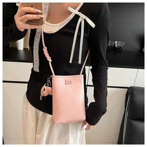 Detailed close-up of pink leather phone bag with embossed m logo and elephant charm accessory