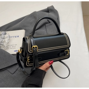 Close-up of black structured handbag featuring gold rivet details and metallic buckle clasp
