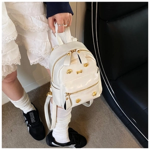Detailed macro view of white mini PU leather backpack with gold puppy-shaped studs