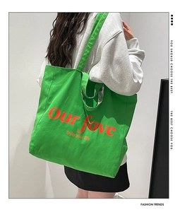 Detail view of large green canvas tote bag with orange graphic print on shoulder