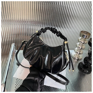 Detail of black glossy cloud bag featuring a ruched handle and sleek oil-wax texture