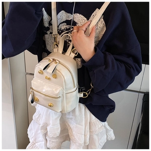 Detailed view of a white patent leather mini backpack featuring golden skull hardware