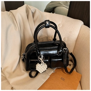 Detail of black glossy Boston bag with pearl heart charm and dual front pockets