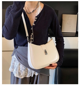 Detail of white leather saddle bag with silver metal buckle on navy blue cardigan