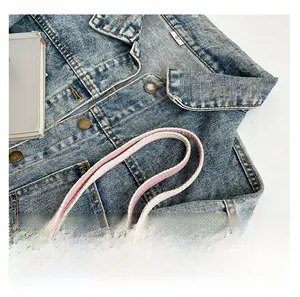 Close-up of blue denim tote bag featuring vintage bronze buttons and pink woven straps