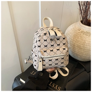 Detail of a beige quilted mini backpack with black bow prints and white straps