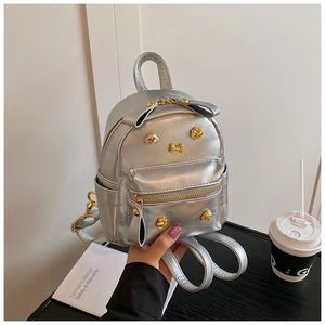 Close-up of mini silver backpack featuring golden dog charms and bow detail