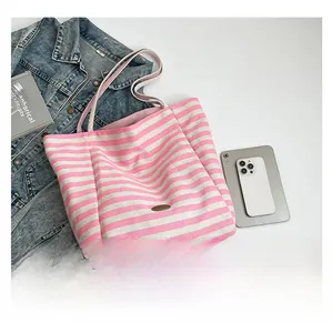 Detail of pink and white striped canvas tote bag with metal nameplate and shoulder strap