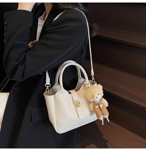 Dettaglio borsa a secchiello in pelle crema con chiusura dorata e ciondolo a forma di orso